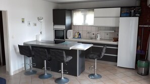 A modern kitchen with a central island, bar stools, a microwave, and a refrigerator. - Apartments Tamara (Solta)