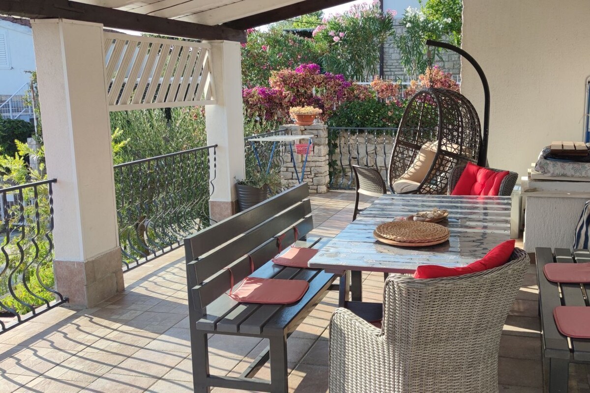 A covered outdoor patio with a table, chairs, and a wicker chair.