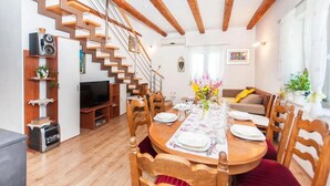 Una sala de estar moderna con una escalera de madera, una mesa de comedor preparada para cuatro personas y un televisor en una esquina.