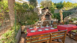 Un espacio de comedor al aire libre con paredes de piedra, un horno de ladrillo y mobiliario de madera.
