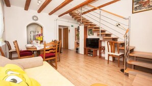Amplia sala de estar con una escalera de madera, una mesa de comedor con sillas, un sofá y un televisor.