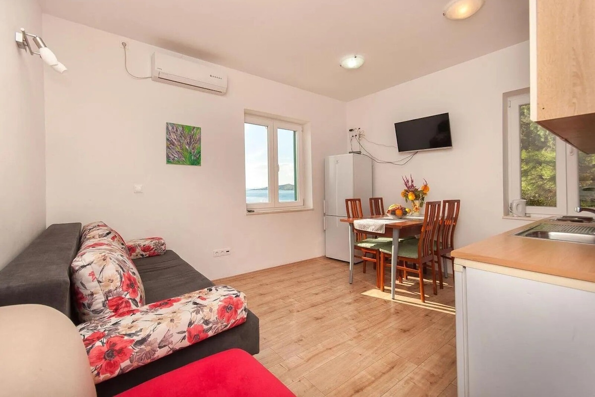 A compact living space with a sofa, a dining table with chairs, a small kitchen area, and a TV mounted on the wall.