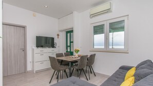 A modern living room with a grey sofa, a dining table with chairs, a TV, and a green door. - Apartment Garden by the Sea (Celina)