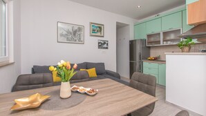 A modern kitchen with green cabinets, a dining area with a wooden table, and a sofa with yellow cushions. - Apartment Garden by the Sea (Celina)