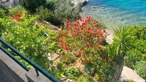 A balcony with a view of the sea, surrounded by greenery and a chair. - Apartment Garden by the Sea (Celina)