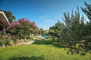 A well-maintained garden with a swimming pool, a stone wall, and a variety of trees. - Villa Flower Garden With Pool (Donji Prolozac)