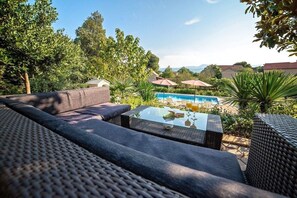 An outdoor seating area with a pool, surrounded by greenery and a clear sky. - Villa Flower Garden With Pool (Donji Prolozac)