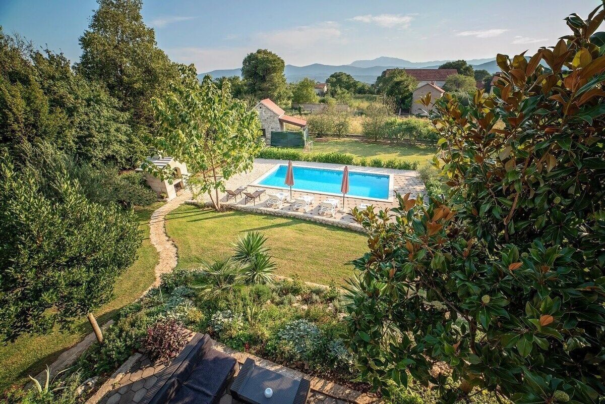 Une piscine entourée d’un jardin, avec un chemin de pierre menant à une maison.