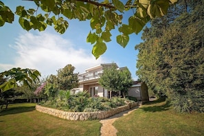 A two-story house with a stone pathway leading to the entrance, surrounded by lush greenery and a well-maintained lawn. - Villa Flower Garden With Pool (Donji Prolozac)