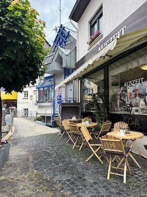 A café with outdoor seating, a blue metal staircase, and a building with a sign reading 'Kleine AUSZEIT'.