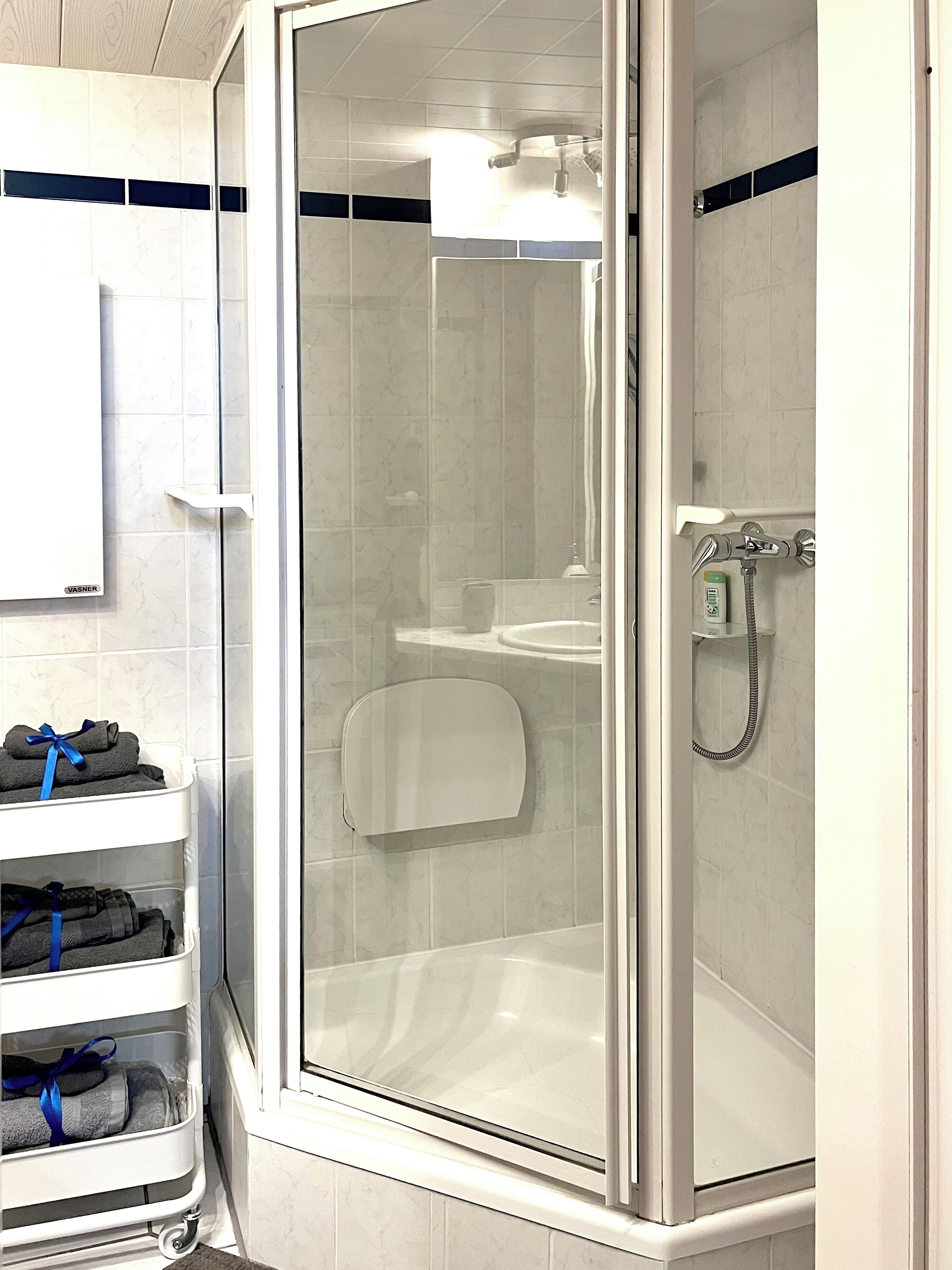 A shower with a glass door, a white sink, and a towel rack with towels.