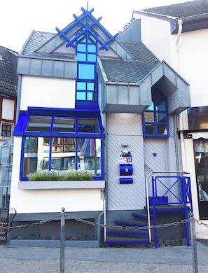 A building with a unique architectural design, featuring a prominent blue cross structure on the roof, multiple windows, and a small outdoor seating area.