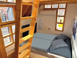 A bunk bed with a ladder, a bed with blue bedding, and a poster on the wall.