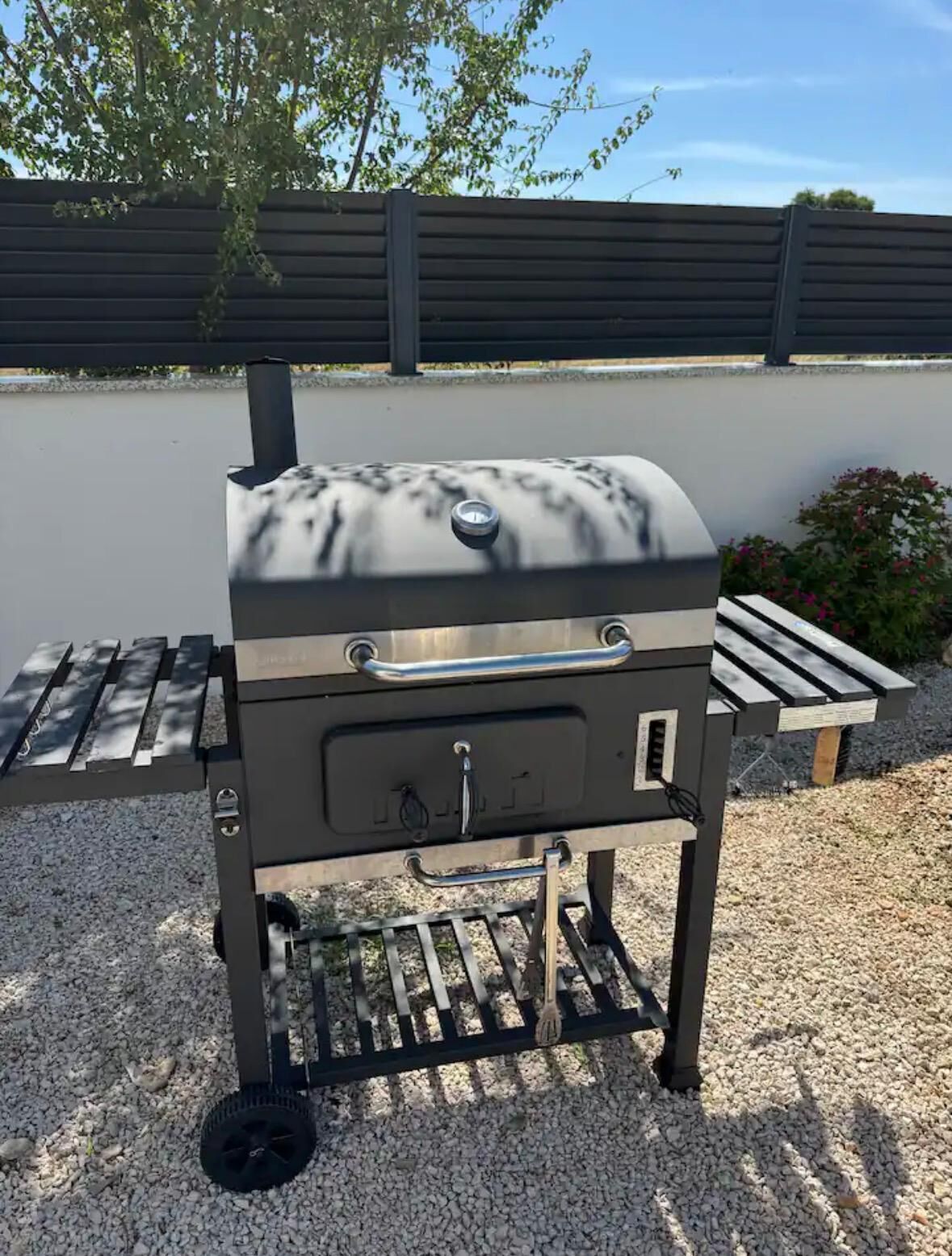 En portabel grill med ett förvaringsutrymme med låda på framsidan, hjul och en skorsten.