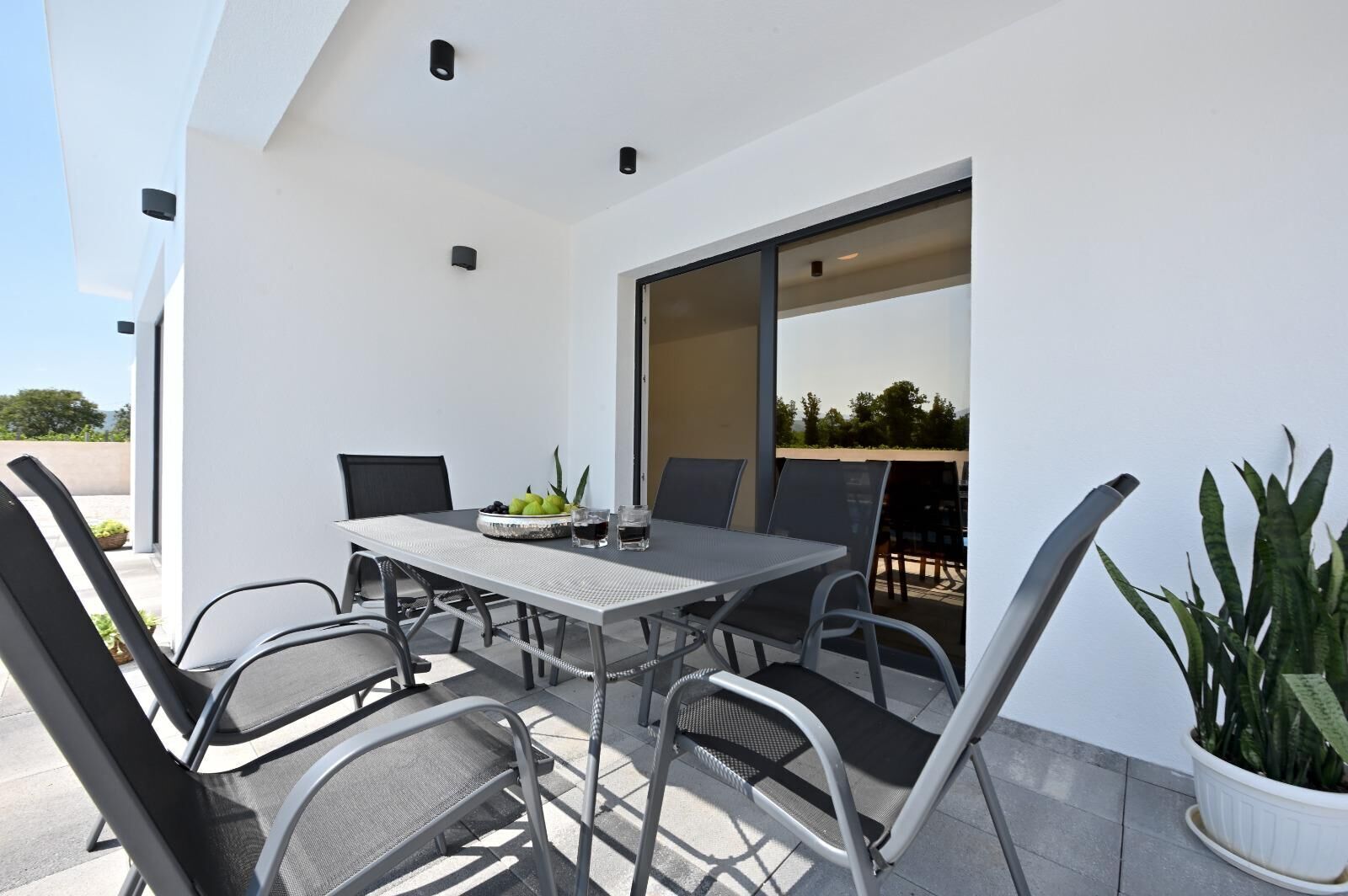 An outdoor patio with a table and chairs, a potted plant, and a view of the outdoors.