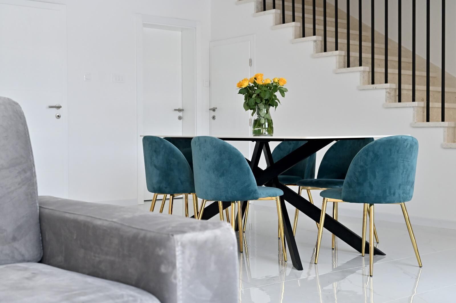 A modern dining area with a black table, teal chairs, and a vase of yellow flowers.