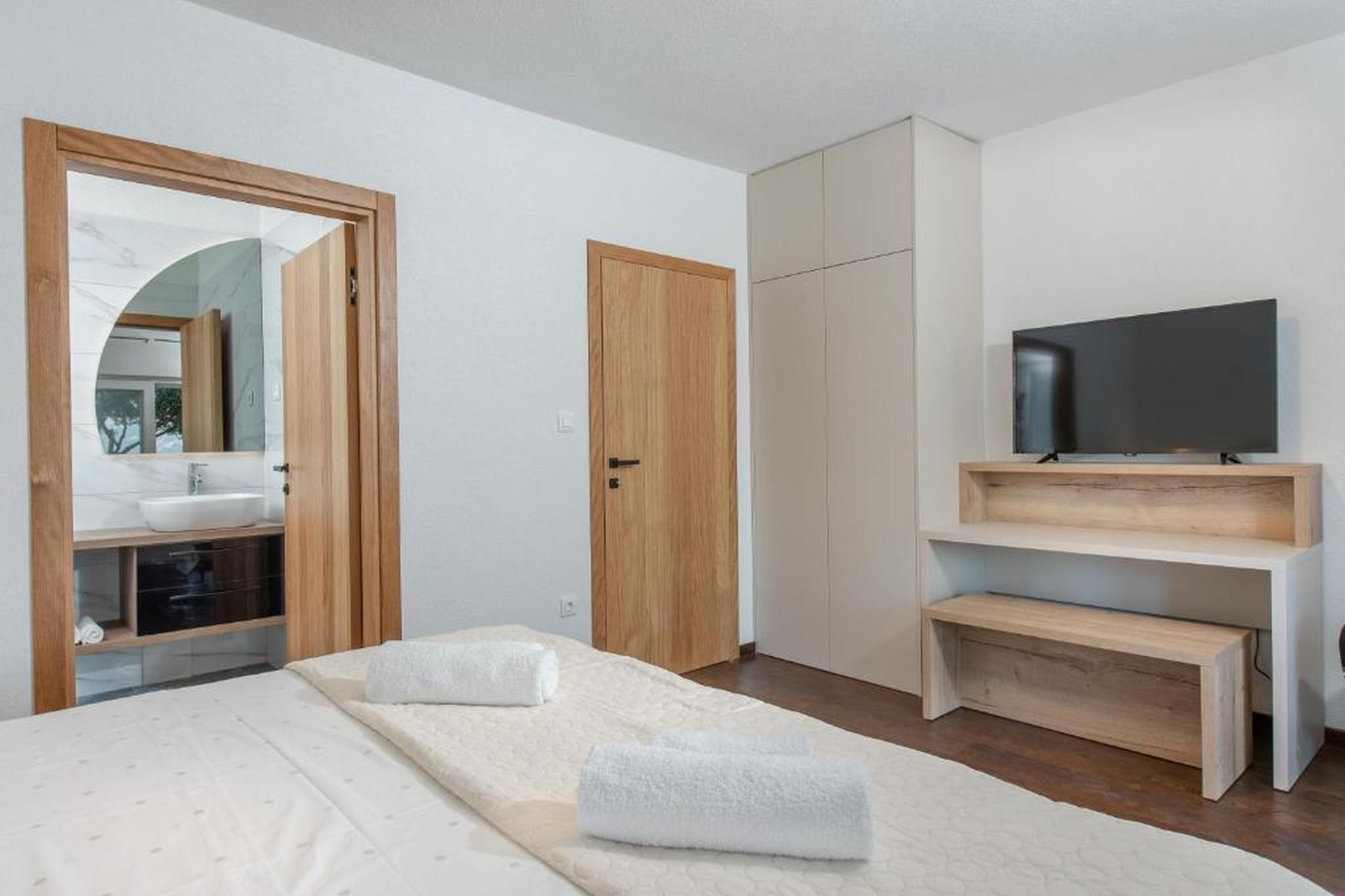 A bedroom with a bed, a TV, a wooden wardrobe, and a mirror.