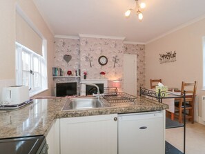 A compact kitchen with a sink, a toaster, a refrigerator, and a dining area with a chair and table. - Wards Court 1, Frampton On Severn (Gloucester)