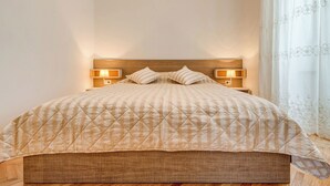 A bed with a quilted headboard, two bedside lamps, and a window with sheer curtains. - Apartment Oscar (Split)