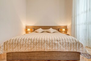 Ein Bett mit gestepptem Kopfteil, zwei Nachttischlampen und einem Fenster mit durchsichtigen Vorhängen.