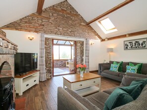 Ein gemütliches Wohnzimmer mit Steindecke, Kamin, Fernseher, einer Couch mit gemusterten Kissen und einem großen Fenster.