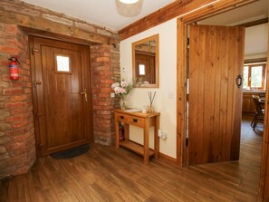Eine Holztür mit kleinem Fenster, eine Ziegelwand, ein Holzkonsolentisch mit einer Vase und ein Spiegel an der Wand.