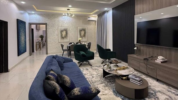 A modern living room with a blue sofa, a round coffee table, and a large TV. - Nouveau Apartment (Abuja)