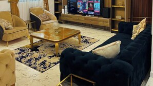 A modern living room with a sofa, armchairs, a coffee table, a TV, and a bookshelf. - Nouveau Apartment (Abuja)
