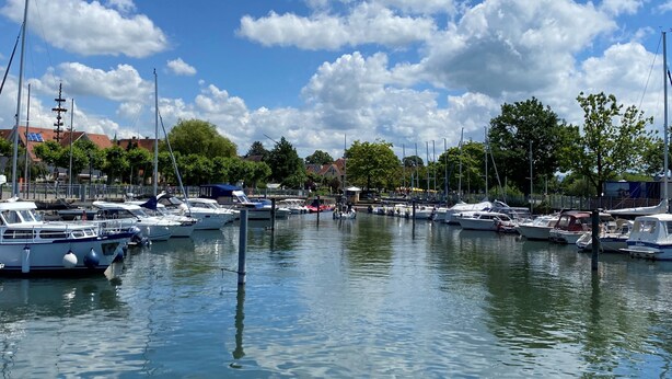 Ein Yachthafen mit mehreren vertäuten Booten, ruhigem Wasser und einem wolkenlosen Himmel.
