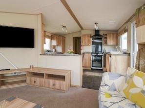 A compact RV interior with a kitchenette, a flat-screen TV, a sofa, and a wooden entertainment unit. - A La Mer is in Paignton, Devon (Paignton)