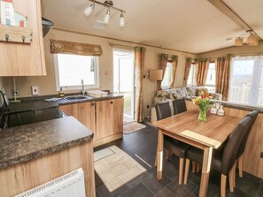 A compact kitchen with a dining area, wooden cabinets, and a window with curtains. - A La Mer is in Paignton, Devon (Paignton)