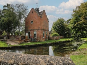 A brick building with a shop sign, a canal, and greenery.