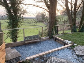 Eine Holzterrasse mit einer Bank, einem Kiesbereich und Blick auf ein grünes Feld.