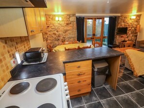 A kitchen with a stove, wooden cabinets, a dining table, and a stone wall. - Valley Cottage, Penzance (Penzance)