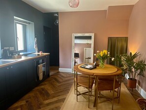 A kitchen with a wooden countertop, a dining table with chairs, a mirror, and a potted plant. - The Balmoral Coach House, Morecambe (Morecambe)