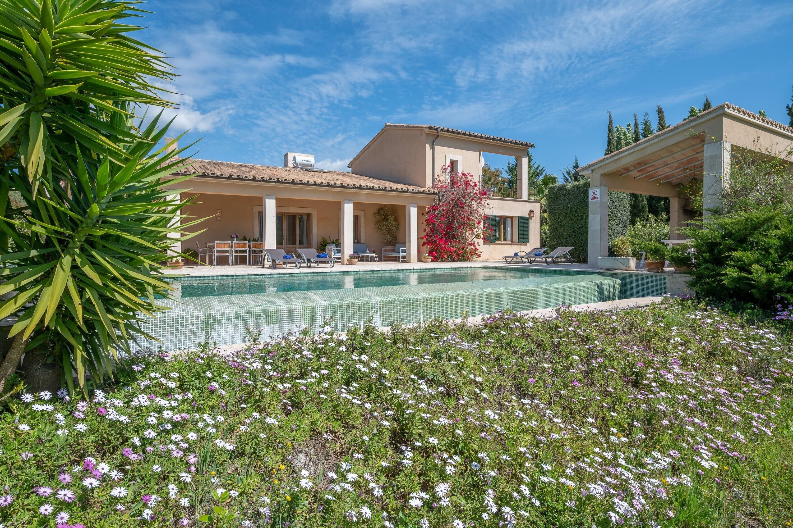 A pool with a tiled edge, a covered outdoor seating area, and a building with a tiled roof.