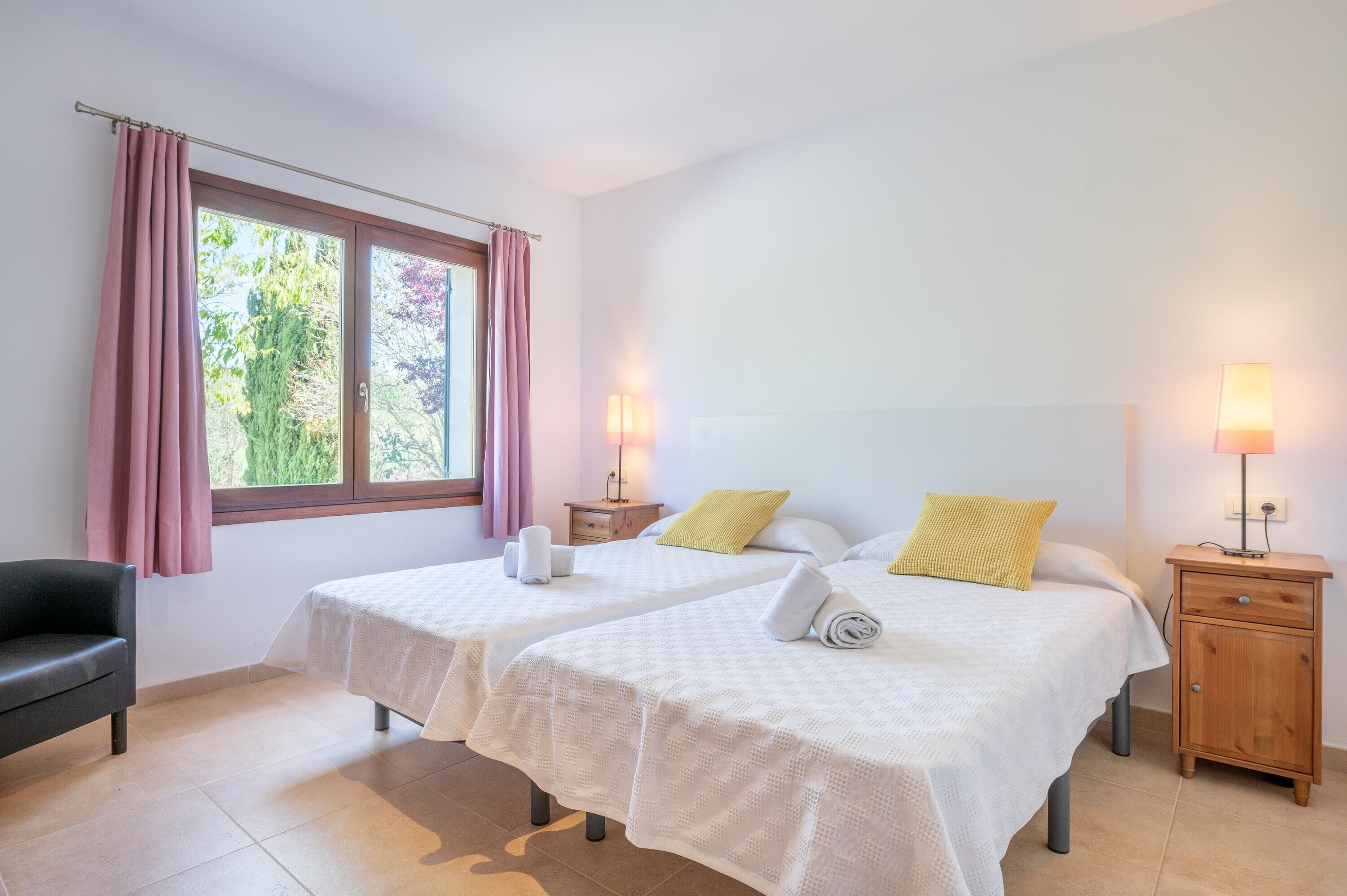 A room with two beds, a nightstand, a lamp, a chair, and a window with curtains.