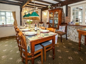 A dining area with a wooden table set for six, flanked by chairs, a green pendant light, and a brick wall with a window.