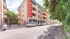 Een meerlaags gebouw met balkons, een hek en een straat met geparkeerde auto's.