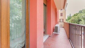 Een balkon met een rode muur, een schuifdeur en een kleine airconditioning.