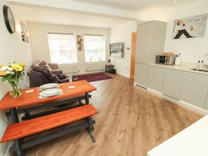Una sala moderna con una mesa de comedor de madera, un sofá y una zona de cocina con armarios y encimera.
