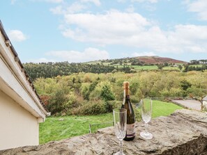 A bottle of champagne and two glasses on a stone ledge with a view of a green landscape and hills. - The Hayloft, Bodelwyddan (Abergele)
