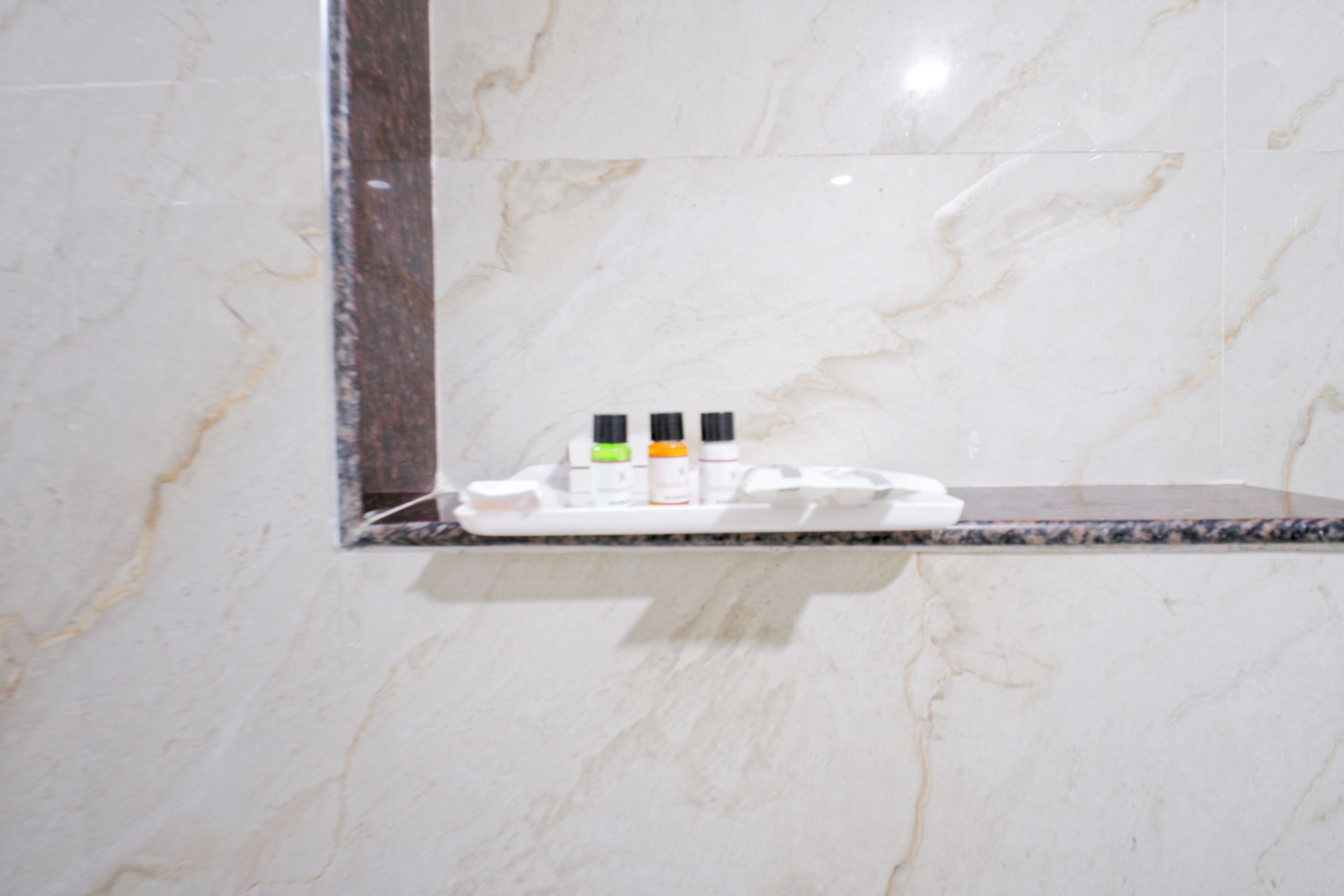 Un baño con pared de mármol, espejo y estante con artículos de aseo.