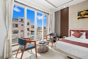 A hotel room with a large window, a bed with white bedding, two chairs, a small round table, and a painting on the wall. - Continente Inn (Faizabad)