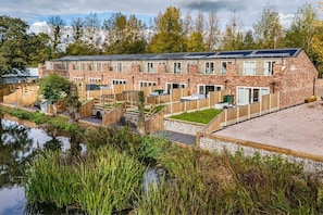 A row of brick buildings with solar panels, a pond, and wooden fences. - 2 Riverside Mews, Borrowwash (Derby)