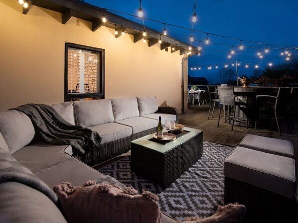 A cozy outdoor seating area with a sofa, a coffee table, and string lights.