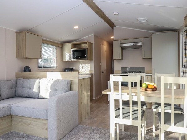 Un espace de vie compact comprenant un canapé, une table à manger avec des chaises, un coin cuisine avec un four à micro-ondes et une cuisinière, et une petite fenêtre.