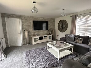 Ein Wohnzimmer mit Flachbildfernseher, Couchtisch, Sofa und dekorativer Wanduhr.