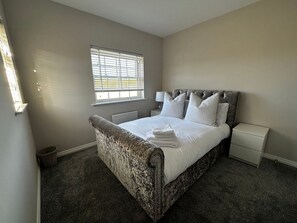 Ein Schlafzimmer mit einem großen Bett, einem Nachttisch, einer Lampe, einem Fenster mit Jalousien und einer Heizung.