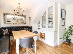 A dining area with a wooden table, black chairs, a black sofa, a chandelier, and a white cabinet with glass doors. - The Farmhouse in North Walsham (North Walsham)